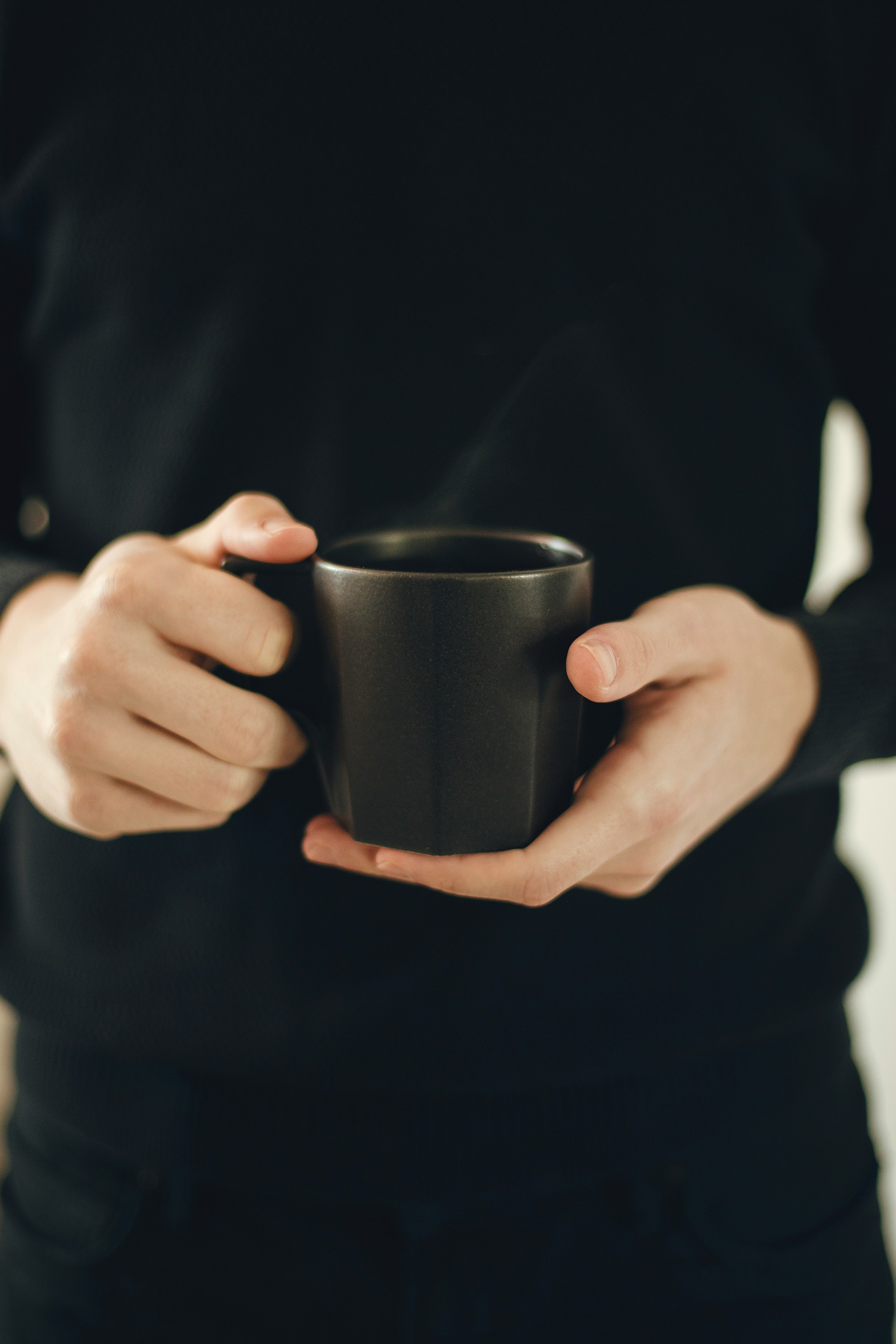 Hands cradle a dark mug in low light
