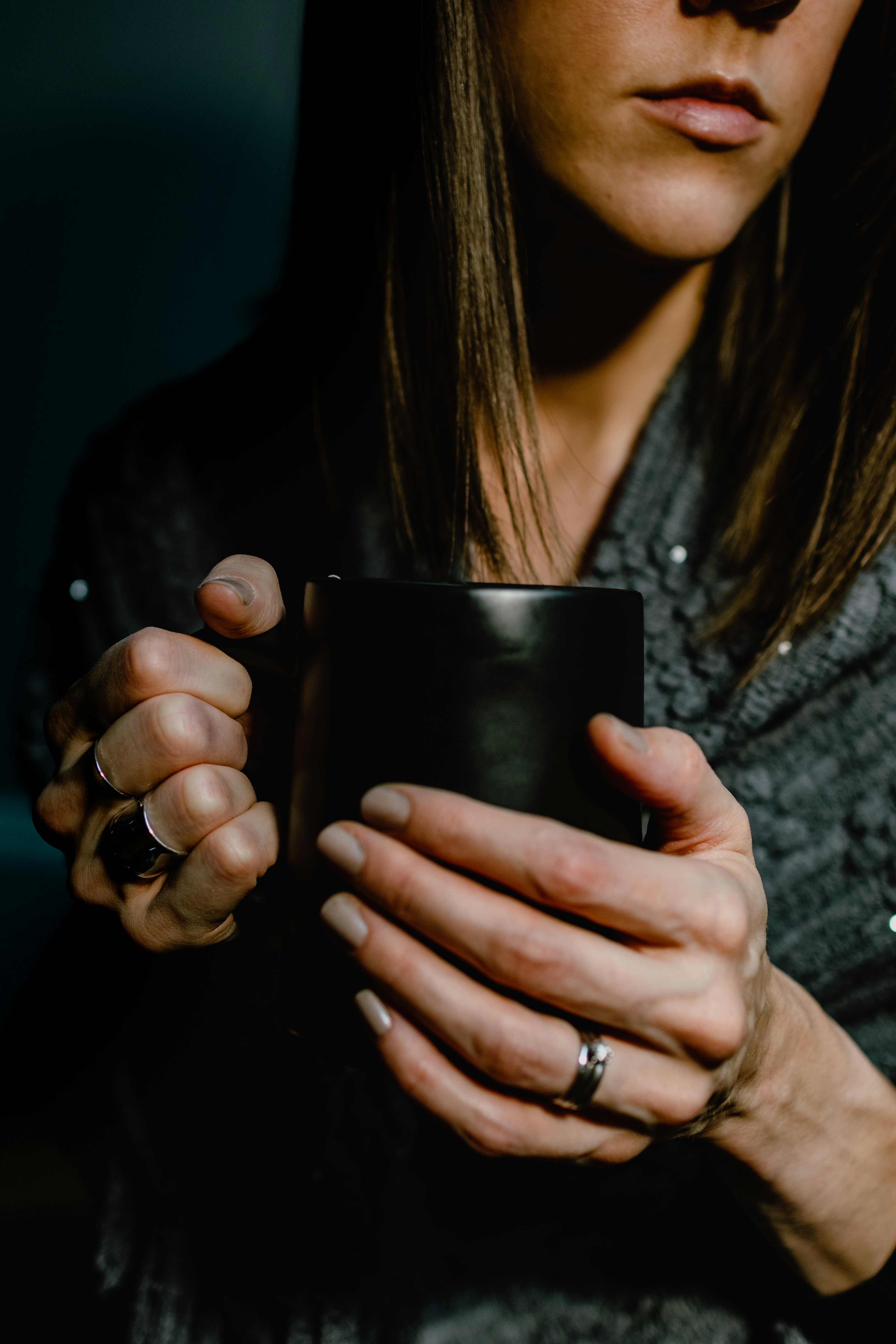 A woman holds a dark mug, partially in shadow