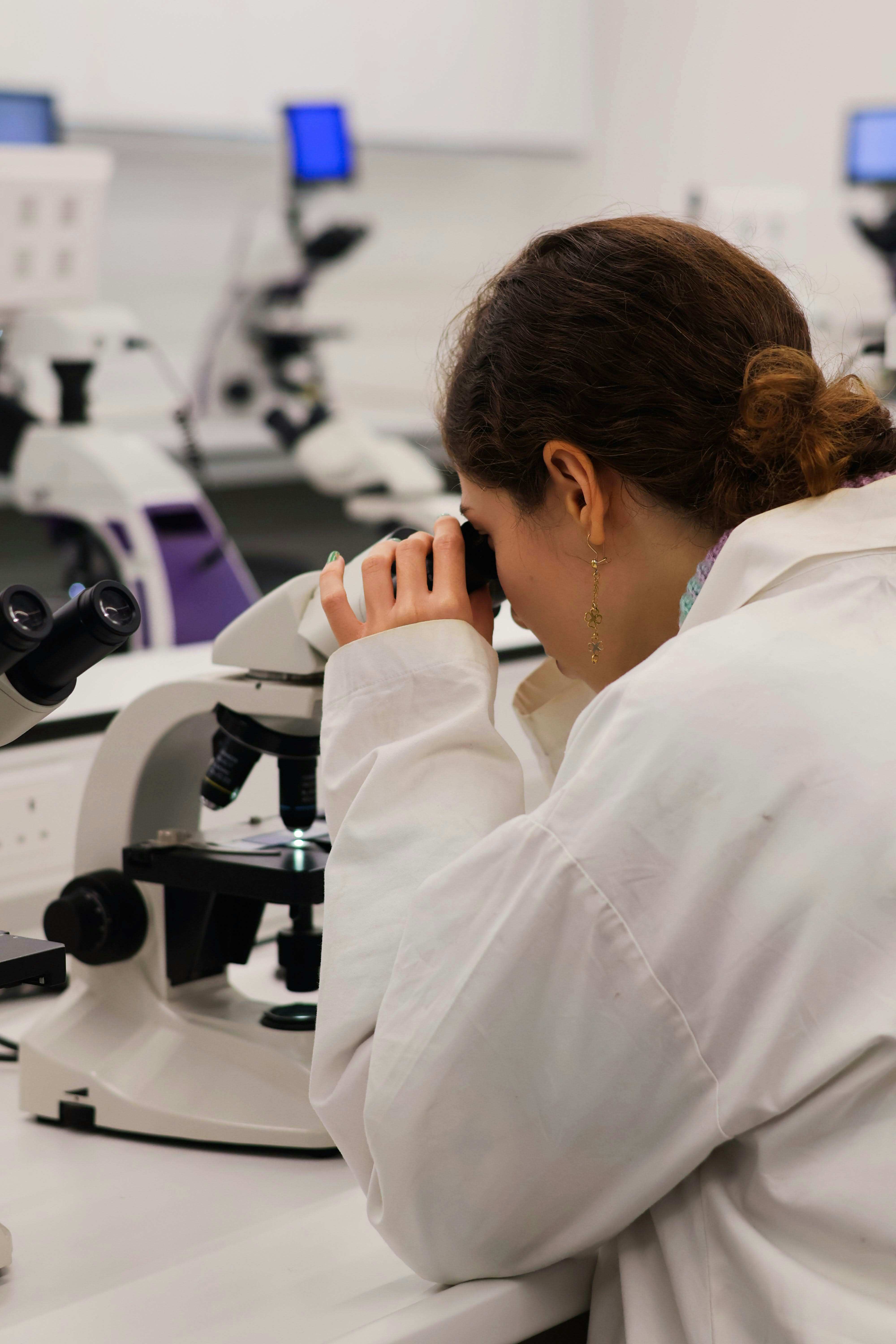 A researcher looks through a microscope in a clinical lab