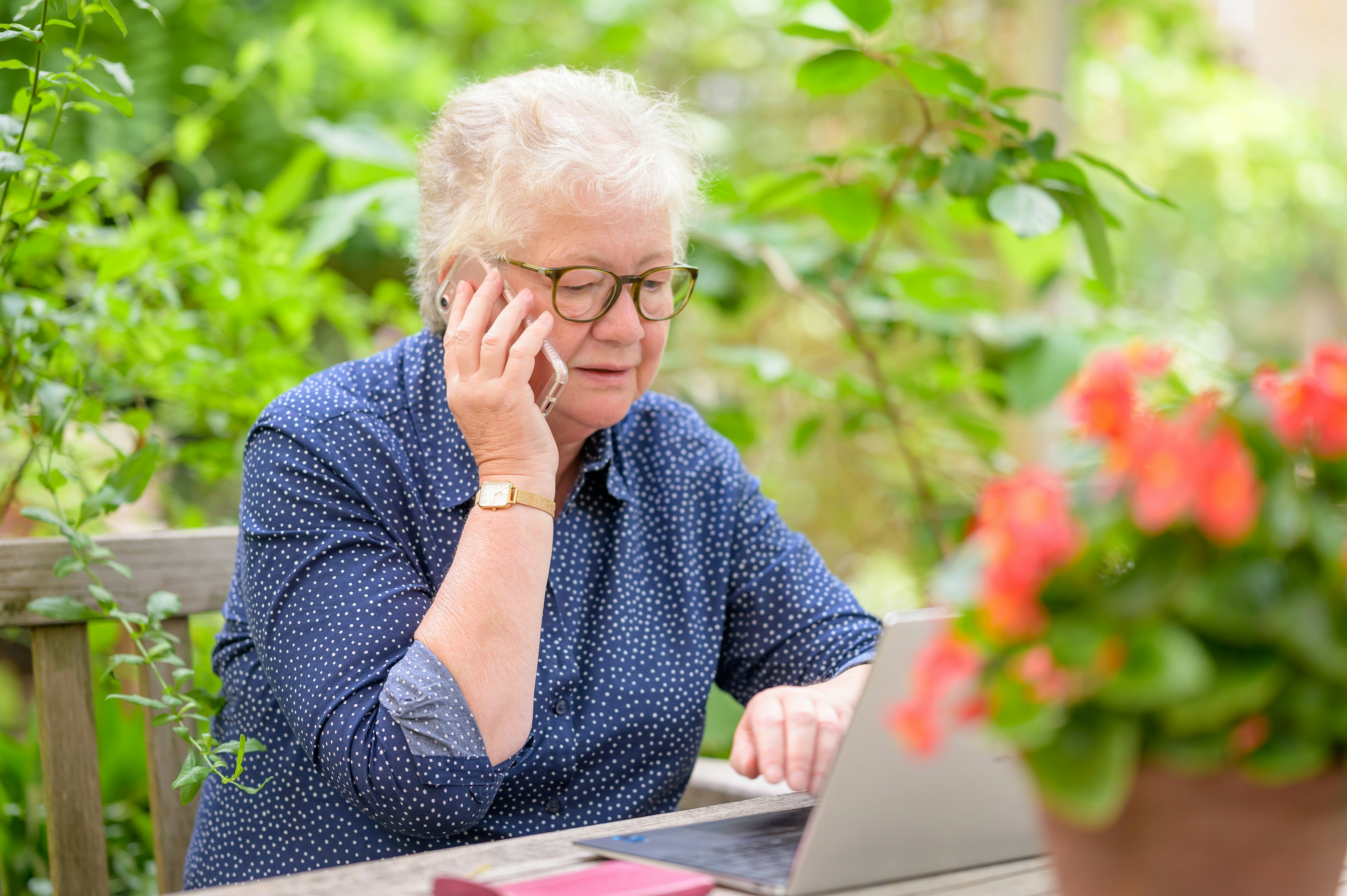 An older woman researches on her laptop while taking a phone call