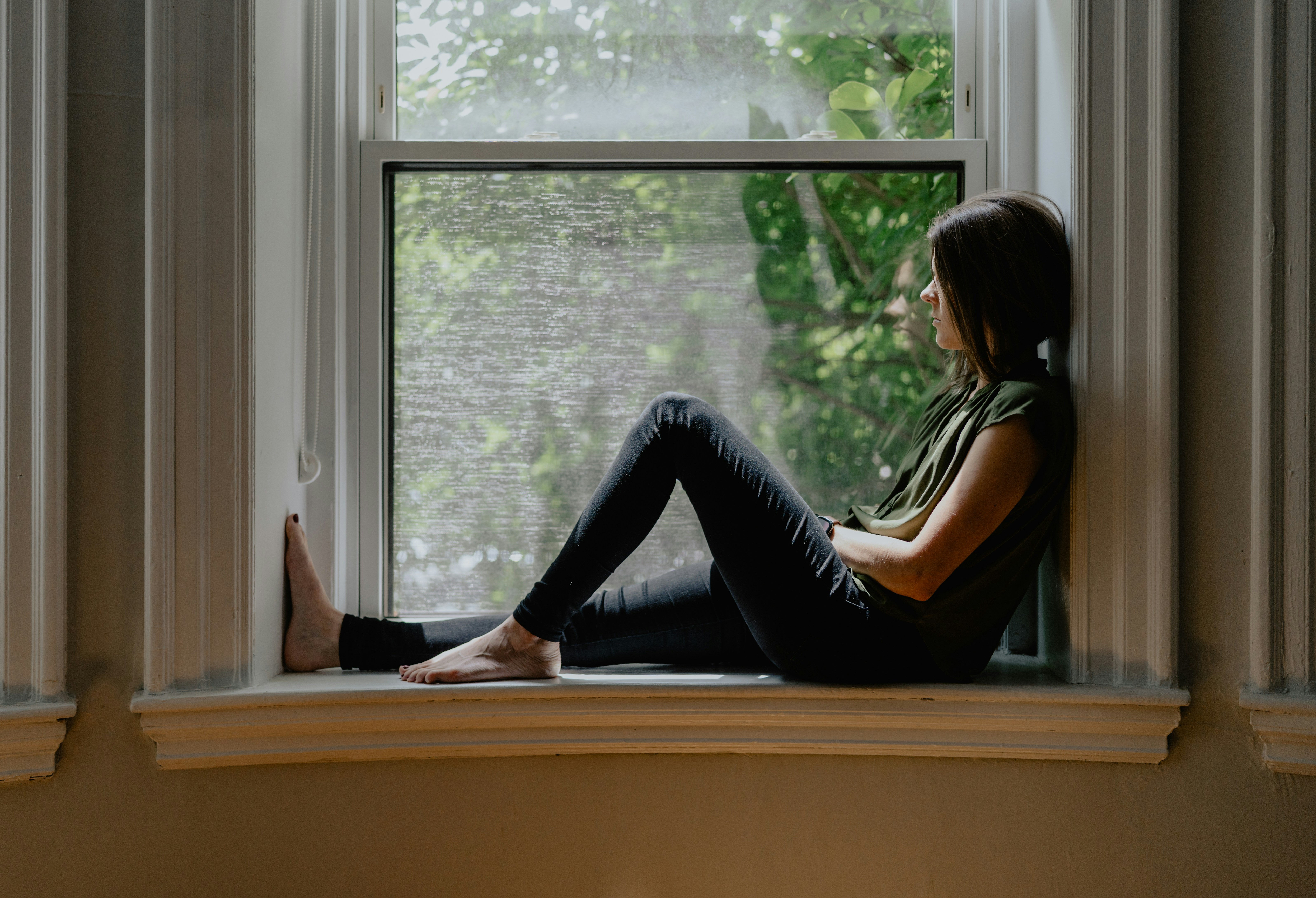 A woman sits quietly by a window, looking outside